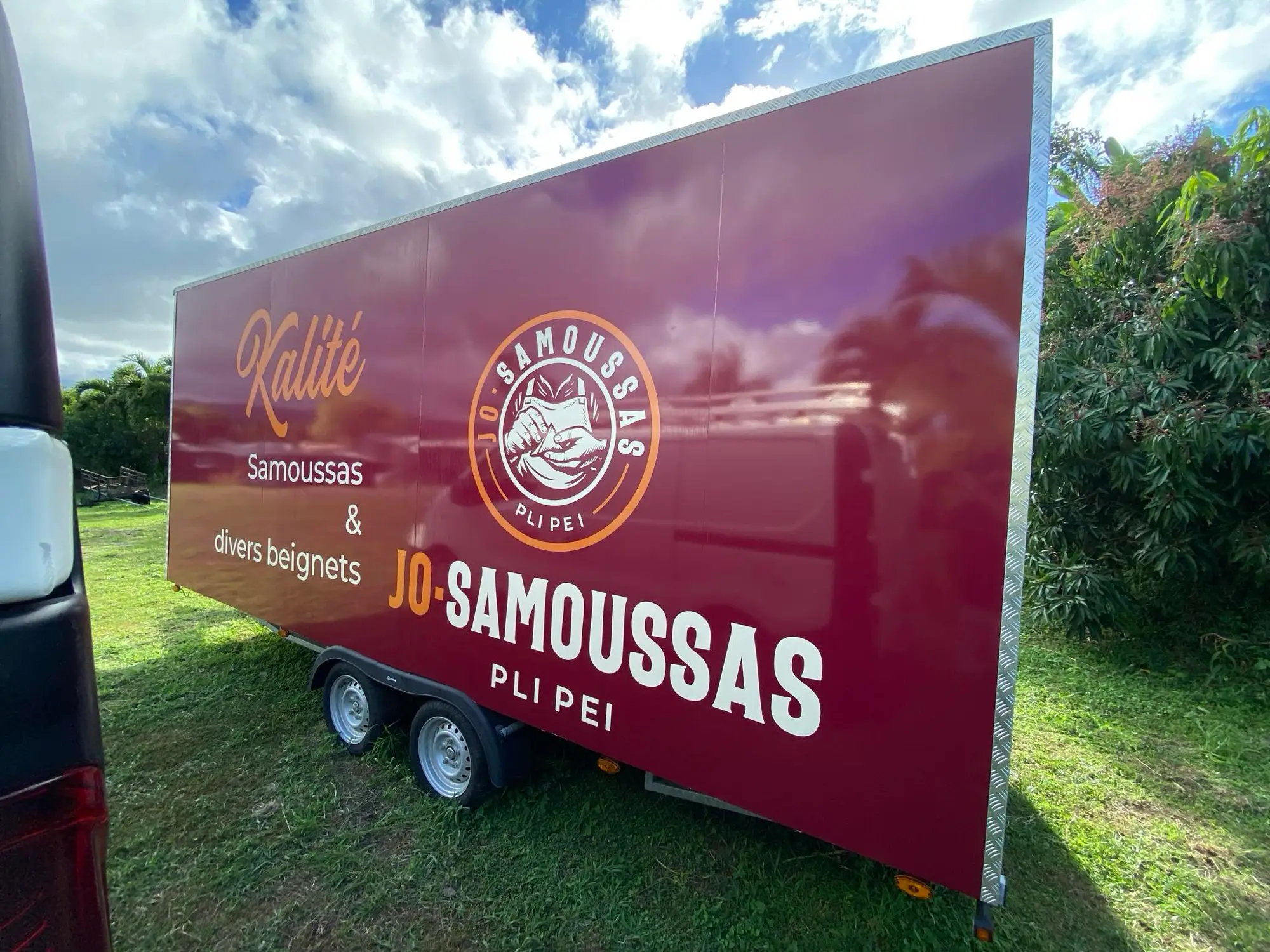 Roulotte de snack habillée en bordeaux avec le logo Jo-Samoussas et l'accroche « Kalité », dans un jardin
