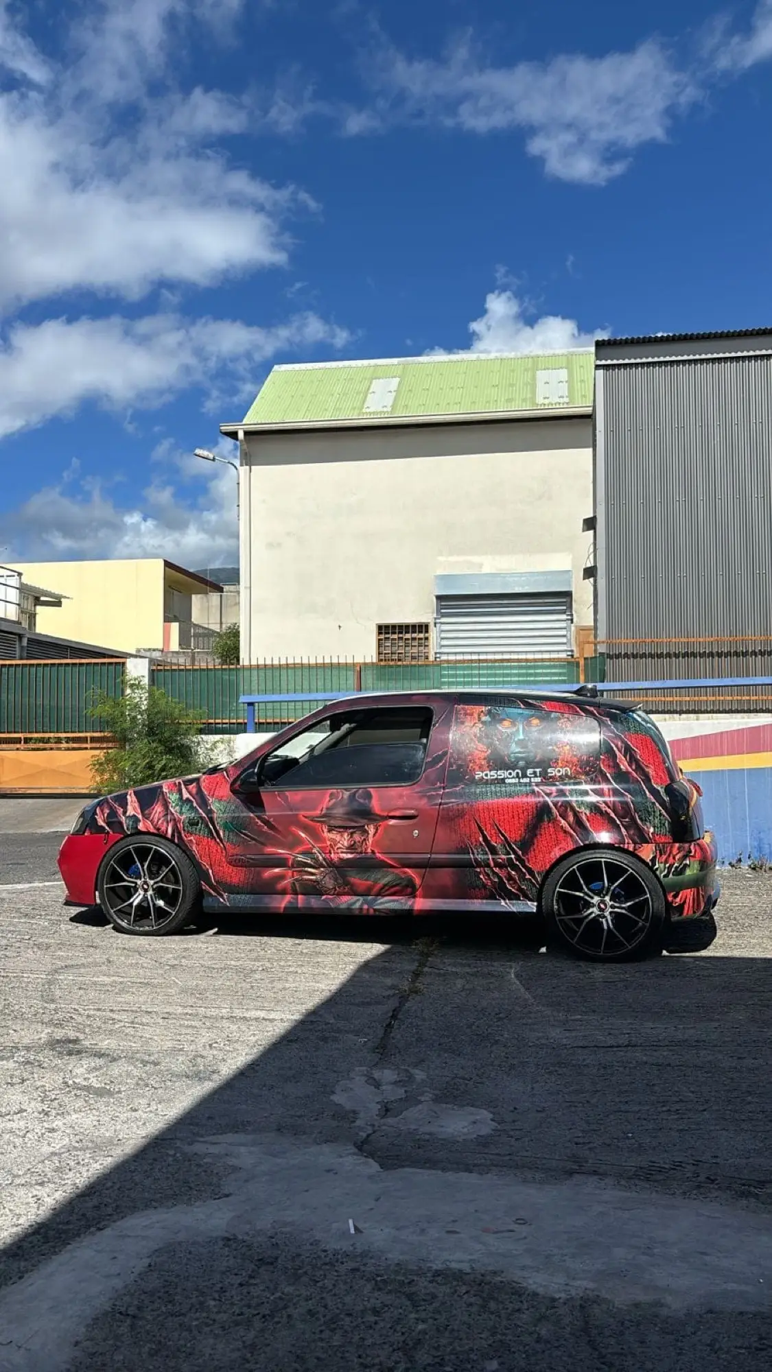 Renault Clio 2 entièrement covérée d'une illustration rouge, verte et noire, vue de trois quarts