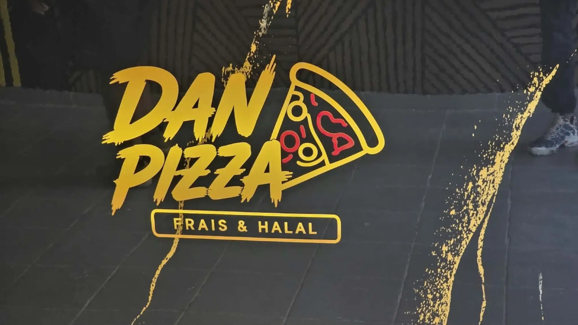 Comptoir noir habillé du logo Dan Pizza en lettrage doré et rouge avec des éclats dorés