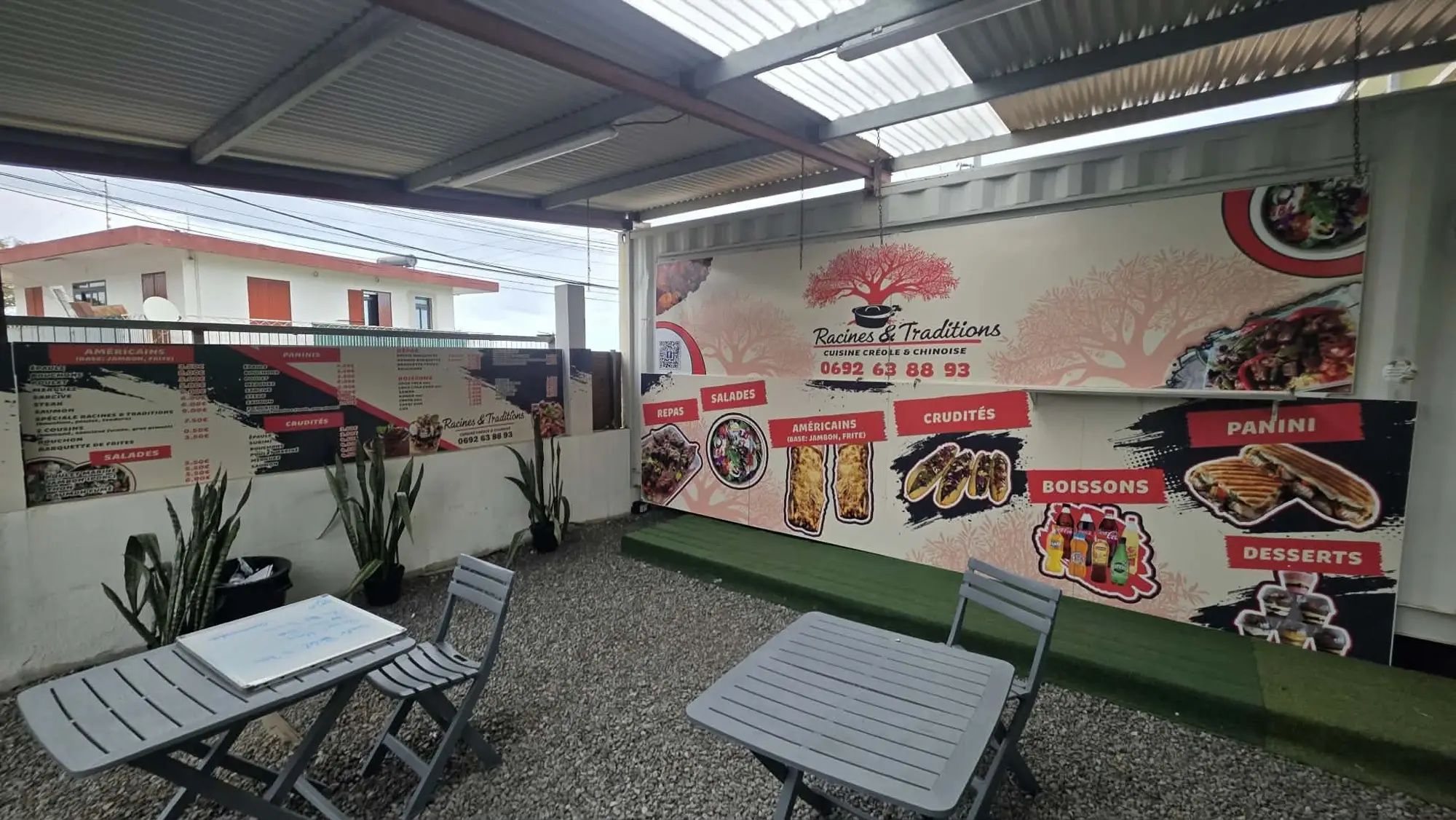 Container de restauration habillé d'un grand visuel menu Racines & Traditions, sous un préau avec tables